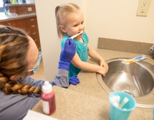 Pediatric dental team member teaching child to brush teeth