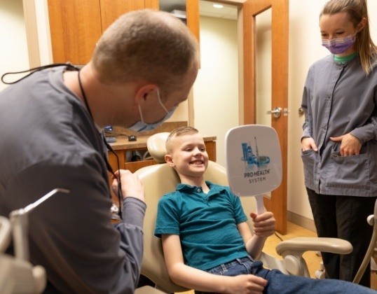 Pediatric emergency dentist and dental team member looking at child after urgent dental treatment