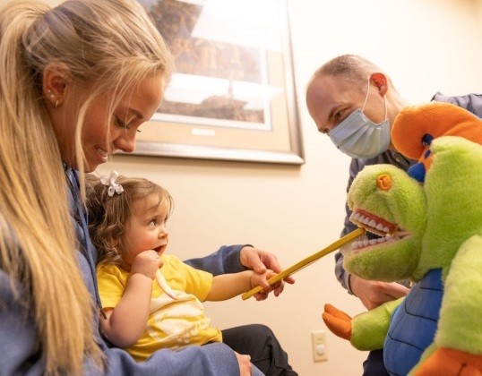 Pediatric dentist teaching child how to brush teeth to prevent dental emergencies