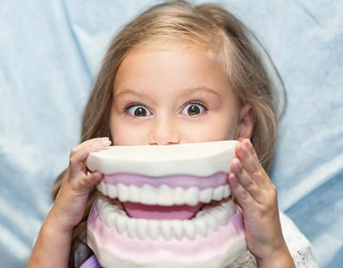 Child holding large model of teeth up