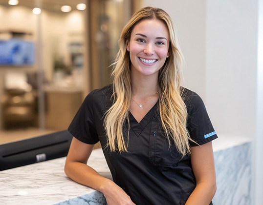 Smiling dental team member leaning against front desk