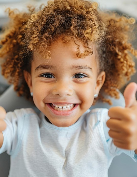 Young child giving two thumbs up while wearing a space maintainer in Castle Rock