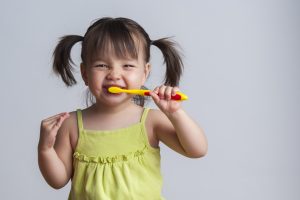 girl yellow shirt brushing teeth