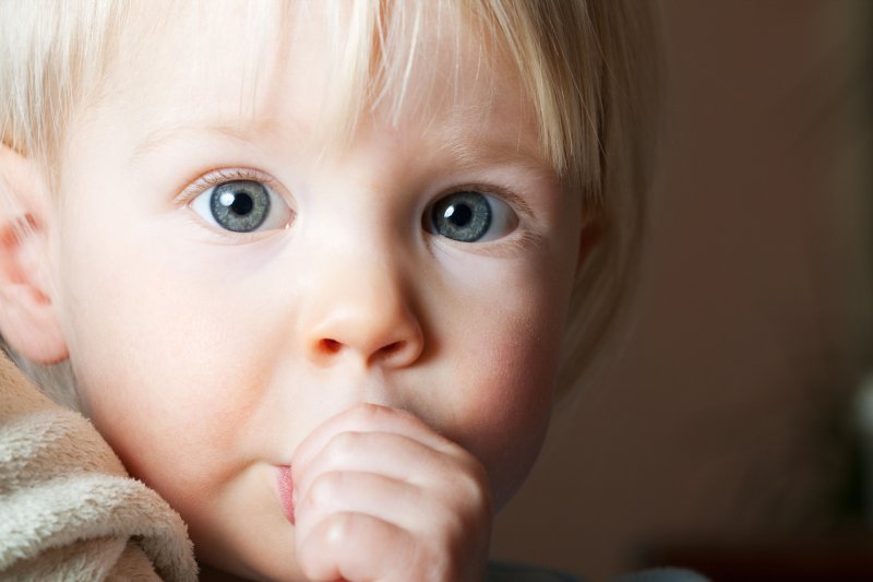 a young child with blue eyes holding a blanket and engaging in thumb sucking