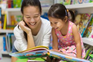 Smiling mother reading her daughter book about visiting the dentist