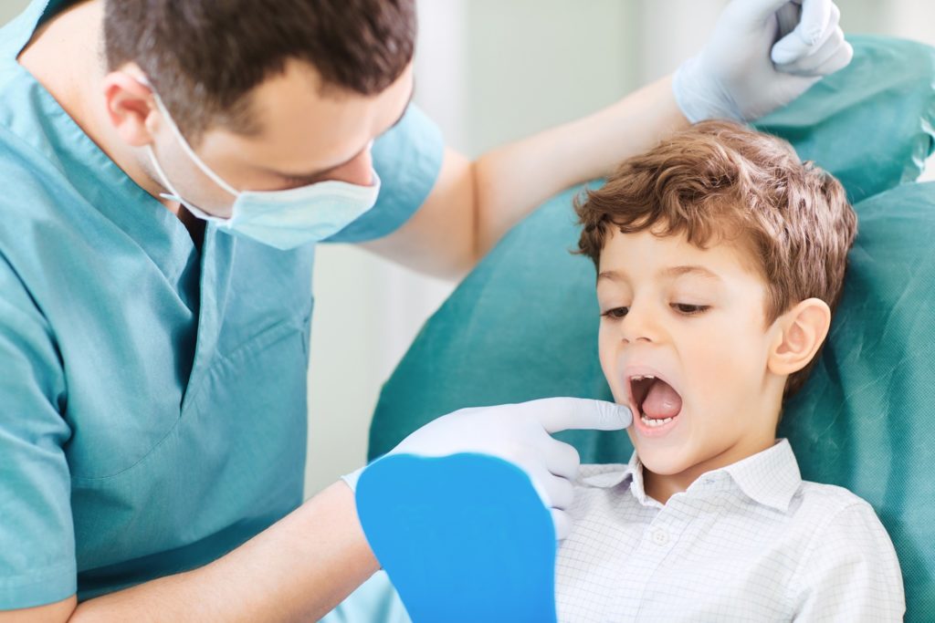 Child looking in mirror as dentist points to their teeth