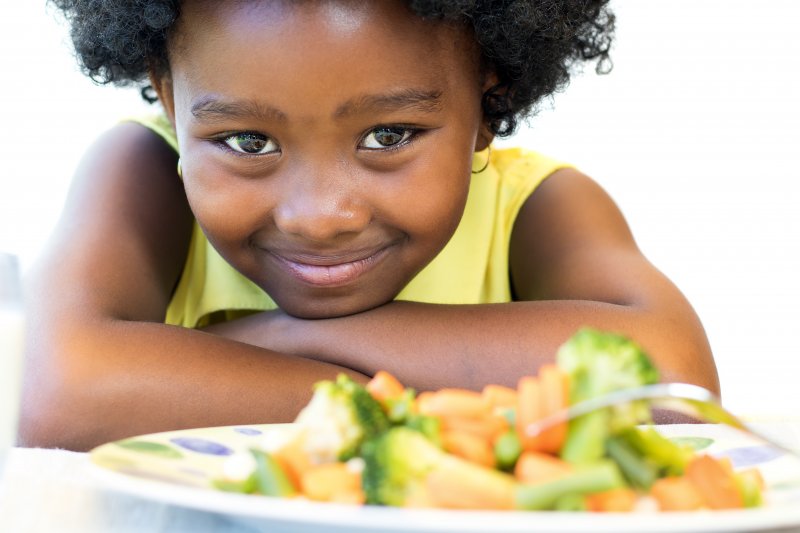 child smiling with vegetables in front of her