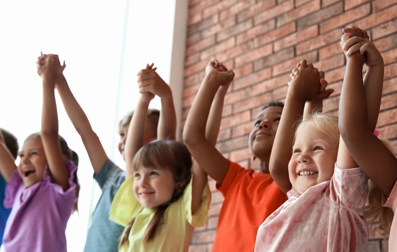 Children smiling with sensitive teeth while holding hands