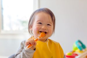 Toddler eating baby food with an orange spoon