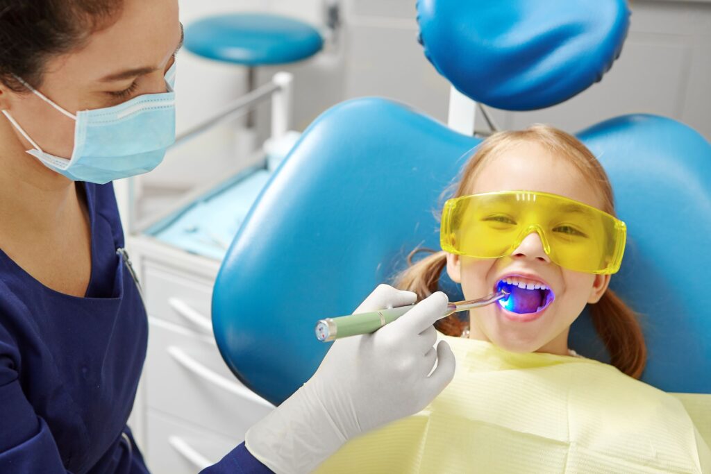Dentist applying UV light to little girls' dental sealant